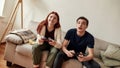 Young couple looking focused, holding game console while playing video games together, sitting on the couch in the Royalty Free Stock Photo