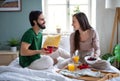 Young couple in love eating breakfast on bed indoors at home, talking. Royalty Free Stock Photo