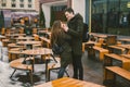 A young couple in love and a girl and a student stand embracing near the tables of a street terrace cafe closed empty without Royalty Free Stock Photo