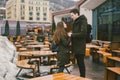 A young couple in love and a girl and a student stand embracing near the tables of a street terrace cafe closed empty without Royalty Free Stock Photo