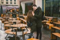 A young couple in love and a girl and a student stand embracing near the tables of a street terrace cafe closed empty without Royalty Free Stock Photo