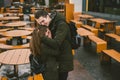 A young couple in love and a girl and a student stand embracing near the tables of a street terrace cafe closed empty without Royalty Free Stock Photo