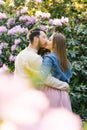 A young couple in love guy and girl kiss on the background of a rhododendron in bloom