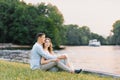 A young couple in love, a guy and a girl are sitting on the shore of the lake, happy and smiling. First date Royalty Free Stock Photo