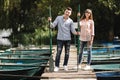 Young couple in love having fun with oars on the wooden bridge. stylish woman and man enjoy canoeing on sunny lake Royalty Free Stock Photo