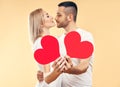 Young couple in love holding big paper hearts in hands over studio background