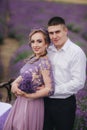 Young couple in love hugging in a lavender field on summer day. girl in a luxurious purple dress