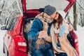 Young couple in love kissing burning sparklers in car trunk in snowy winter forest. People celebrating Christmas Royalty Free Stock Photo