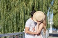 Young couple in love, kissing in park in summer, smiling, hiding behind straw hat. Pretty blond girl in stripy overall on romantic