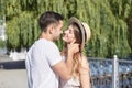 Young couple in love, kissing in the park in summer, smiling, looking at each other. Pretty blond girl in stripy overall and straw Royalty Free Stock Photo