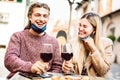 Young couple in love with open face masks having fun at wine bar outdoors - Happy millenial lovers enjoying lunch together at