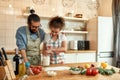 Young couple in love preparing the dough for making pizza with vegetables at home. Man and woman wearing apron, cooking Royalty Free Stock Photo