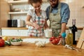 Young couple in love preparing the dough for making pizza with vegetables at home. Man and woman wearing apron, cooking Royalty Free Stock Photo