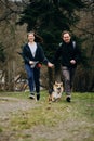 A young couple in love is running around the park with their dog. Girlfriend and boyfriend have fun outside with welsh Royalty Free Stock Photo