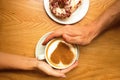 Young couple in love sit in cafe ,hands holding cup of coffee with art heart and 2 donuts on a plate on a wooden table background Royalty Free Stock Photo