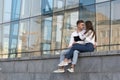 Young couple in love sits outside of building and whispers. Girl is sitting on the lap of guy and hugs him. Student love Royalty Free Stock Photo