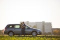 Young couple in love, slim attractive woman with long ponytail and handsome man standing together at silver car in green field on Royalty Free Stock Photo