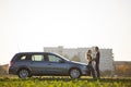 Young couple in love, slim attractive woman with long ponytail and handsome man standing together at silver car in green field on Royalty Free Stock Photo