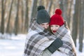 Young couple in love in snow-covered park covered themselves with warm blanket. Man and woman in winter forest