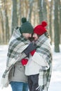 Young couple in love in snow-covered winter park covered themselves with warm blanket. Vertical frame
