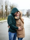 Young couple in love, standing on the park path, wearing hoods, hugging, looking at each other on the rainy spring day. Romantic Royalty Free Stock Photo