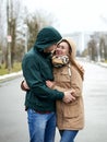 Young couple in love, standing on the park path, wearing hoods, hugging, looking at each other on the rainy spring day. Romantic Royalty Free Stock Photo