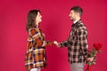 Young couple in love in the studio on a red background hold hands. The man hides the roses behind his back Royalty Free Stock Photo