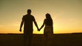 Young couple in love walking across the field holding hands. girl and man go to the sunset. happy family walks in the Royalty Free Stock Photo