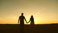 Young couple in love walking across the field holding hands. girl and man go to the sunset. happy family walks in the Royalty Free Stock Photo