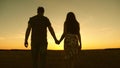 Young couple in love walking across the field holding hands. girl and man go to the sunset. happy family walks in the Royalty Free Stock Photo