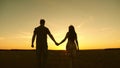 Young couple in love walking across the field holding hands. girl and man go to the sunset. happy family walks in the Royalty Free Stock Photo