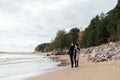 Young couple in love walking on the beach coast. Cold autumn weather, trees in the background. Royalty Free Stock Photo