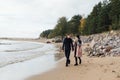 Young couple in love walking on the beach coast. Cold autumn weather, trees in the background. Royalty Free Stock Photo