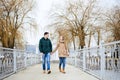 Young couple in love, wearing beige and green casual jackets, holding hands, walking on the lock bridge in winter with yellow