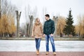 Young couple in love, wearing beige and green casual jackets, standing in front of frozen lake holding each others` hands, lookin Royalty Free Stock Photo