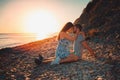 A young couple of lovers embrace sitting on the beach, and pose against the background of the sea and sunset. Side view. The Royalty Free Stock Photo