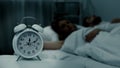 Young couple lying asleep in bed at night with clock standing near, sleep phases