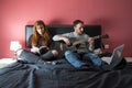 Young couple lying in bed. man lying in bed playing guitar and woman in bed reading Royalty Free Stock Photo