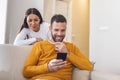 Young couple lying at home. One of them use the phone and flirting. The other person is jealous and spies of the arm. The concept Royalty Free Stock Photo