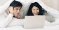 Young couple lying together under blanket on bed enjoy watching movie on laptop computer. Royalty Free Stock Photo