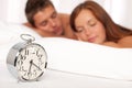 Young couple lying in white bed with alarm clock Royalty Free Stock Photo