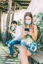 Young couple maintaining social distance in a bank, both wearing a medical mask and using their phone Royalty Free Stock Photo