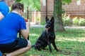 Young couple making photo of big black dog German Shepherd sitting in front of them and looking to the camera smiling. Royalty Free Stock Photo