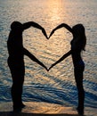 Young couple making shape of heart with arms on beach