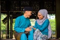 Young couple of malay muslim in traditional costume having happy conversation during Aidilfitri celebration at traditional wooden