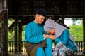 Young couple of malay muslim in traditional costume showing apologize gesture during Aidilfitri celebration at traditional wooden