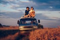 Young couple man with a guitar and woman in a hat are sitting on the roof of a car in a wheat field. Travel and adventur Royalty Free Stock Photo