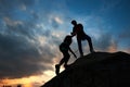 Young couple man and woman climbing on boulder. Helping hand. Silhouettes on sunset background.