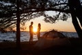 Young couple man and woman having rest at tourist tent and burning campfire on sea shore near forest Royalty Free Stock Photo