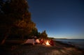 Young couple man and woman having rest at tourist tent and burning campfire on sea shore near forest Royalty Free Stock Photo